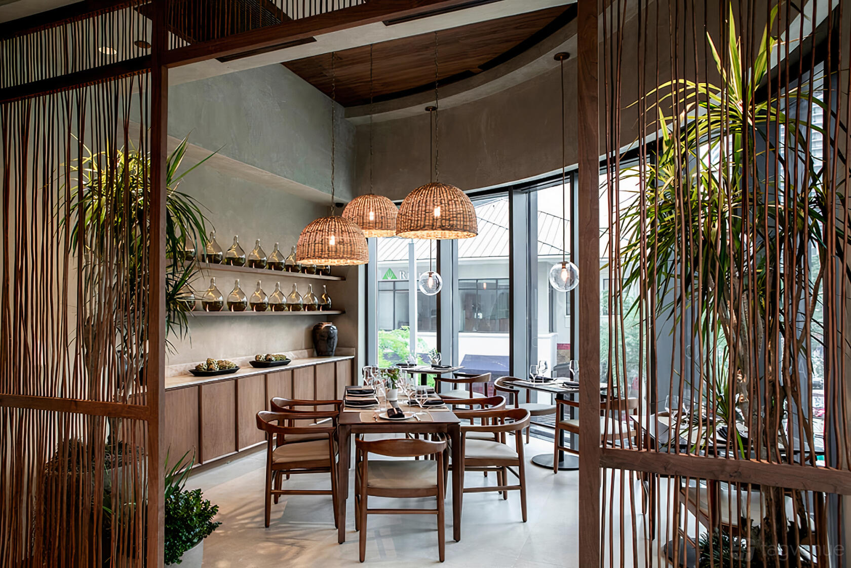 A private dining room with round wooden tables, wicker pendant lamps, and large windows at Kaori.