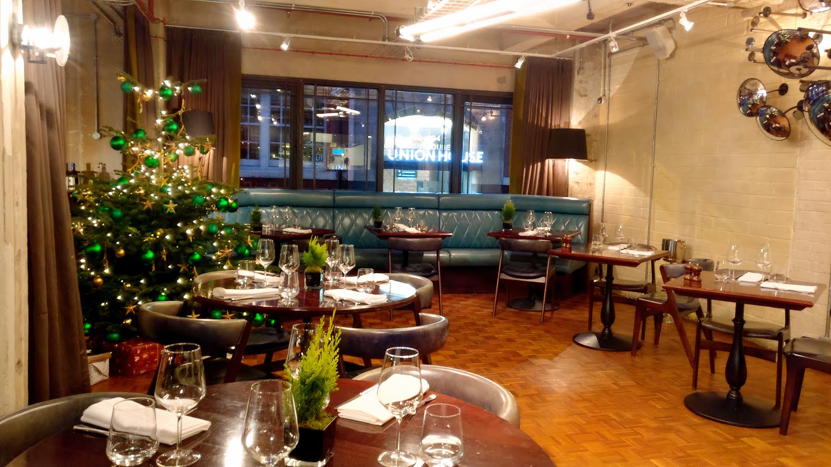 A restaurant with parquet flooring, teal banquette seating, and round tables set for dining at Bread Street Kitchen, Southwark.