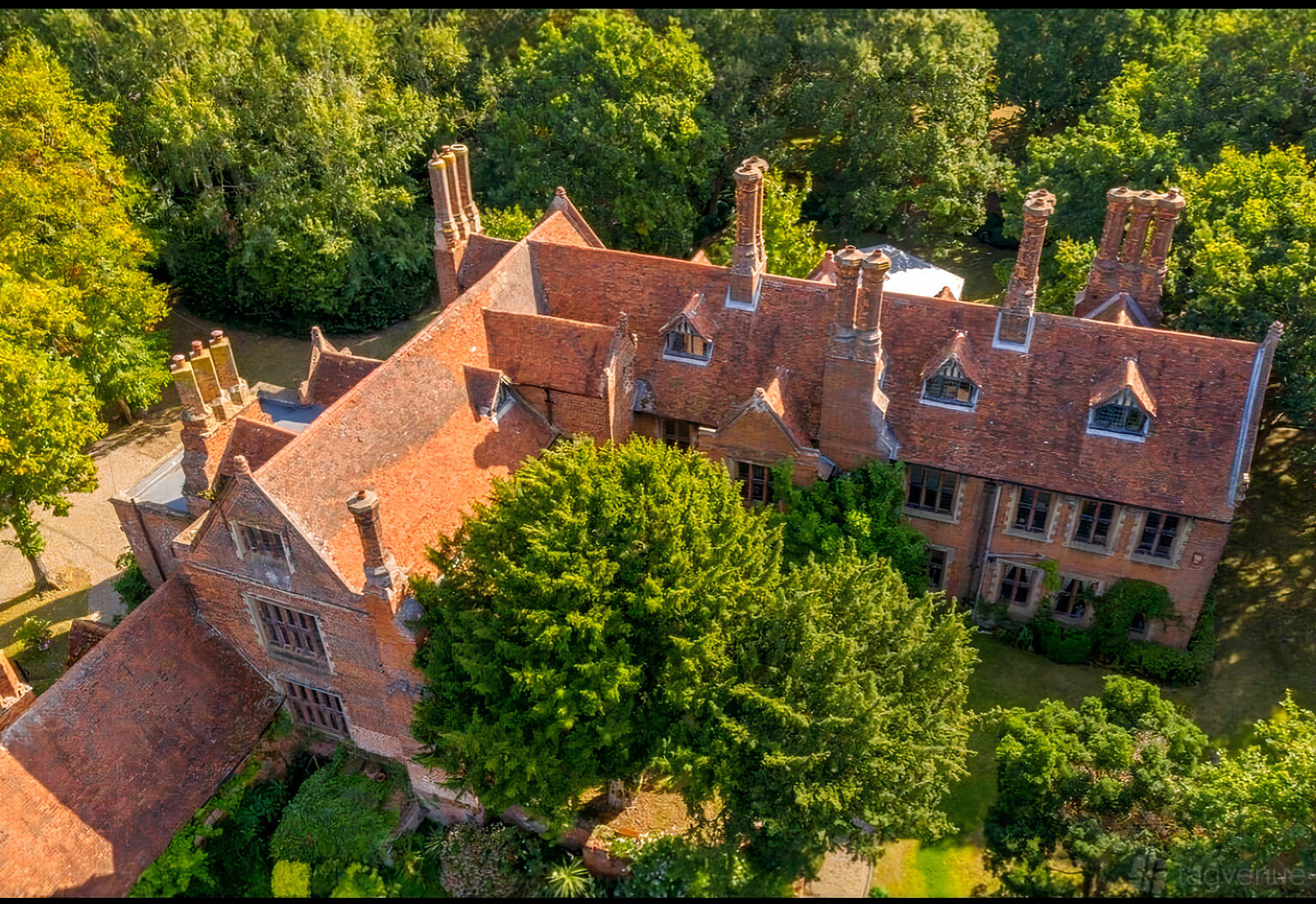 A country house with red tiled roofs, tall chimneys, and mature trees surrounding Creeksea Place.