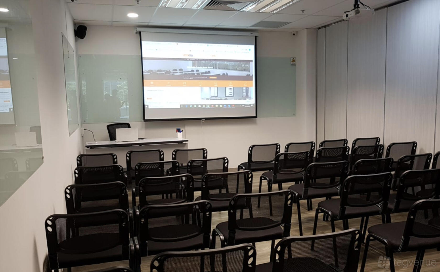 A training room with rows of black chairs facing a projector screen and a whiteboard at Synergy Room Havelock 2.