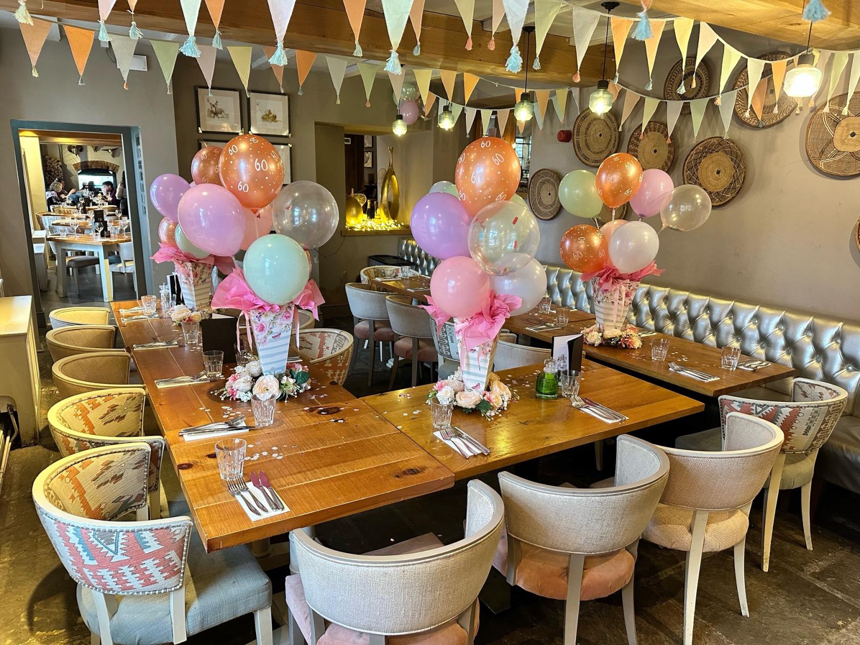 A pub dining room with a long wooden table, pastel balloon centerpieces, upholstered chairs, and bunting at The Ashton.