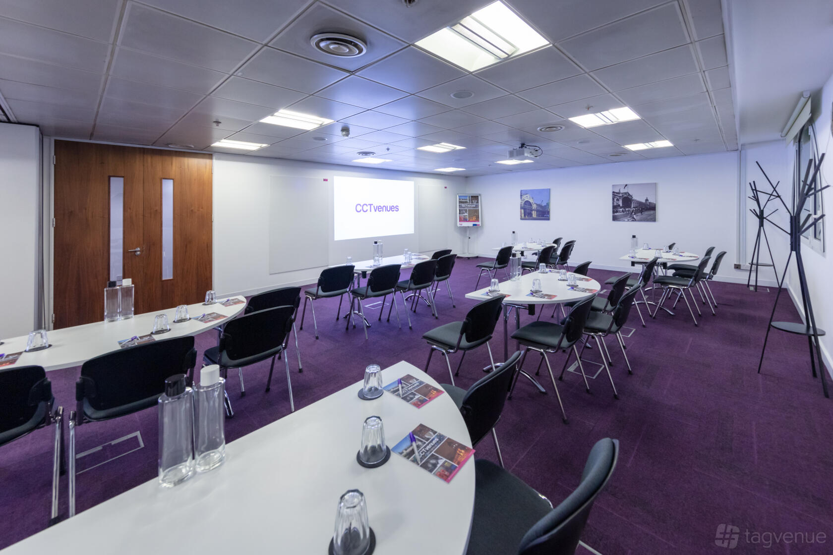 A conference centre with purple carpet, oval tables, projection screen, and coat racks at CCT Venues - Smithfield.