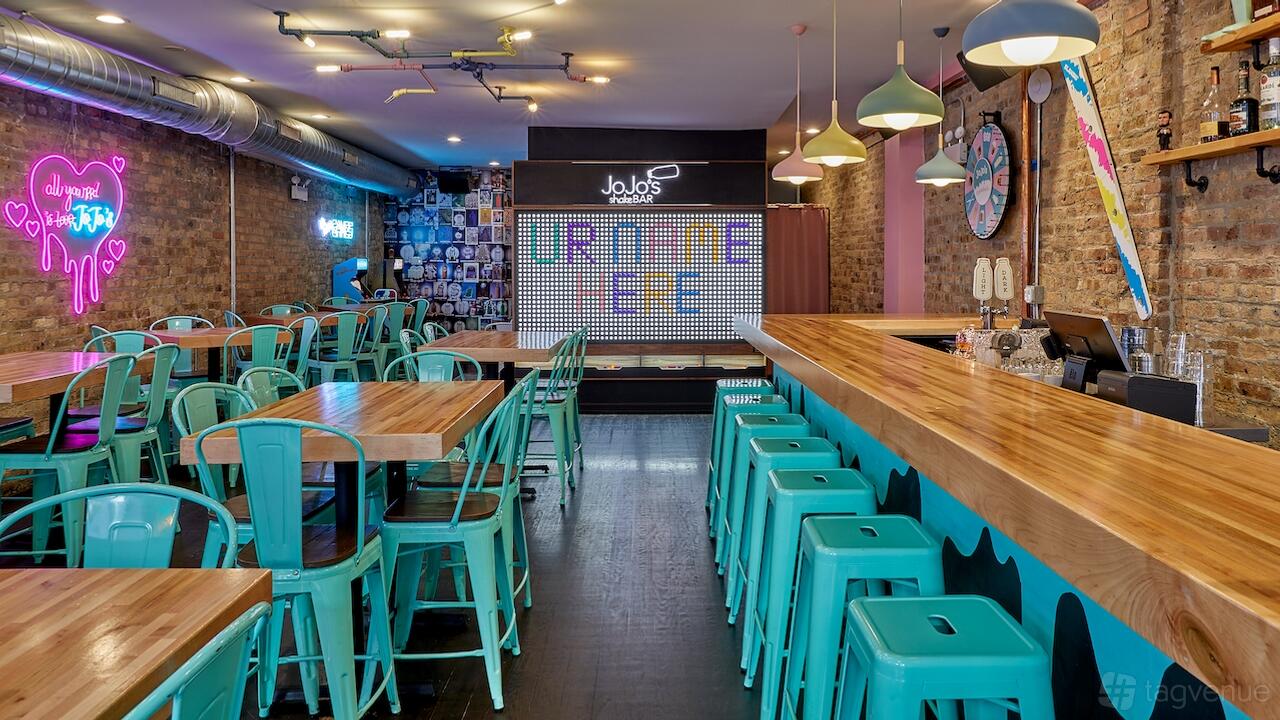 A dining room with exposed brick walls, colorful neon signs, and teal chairs at JoJo's Shake Bar - River North.