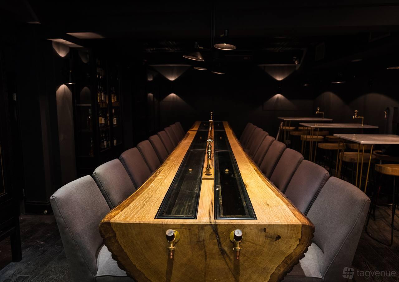 A bar with a long wooden communal table, built-in brass taps, and dim ambient lighting at Black Rock Bar.