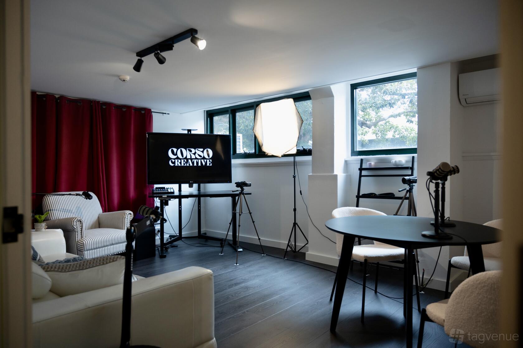 A creative space with lounge chairs, podcast microphones, softbox lighting, and camera equipment at Corso Creative.