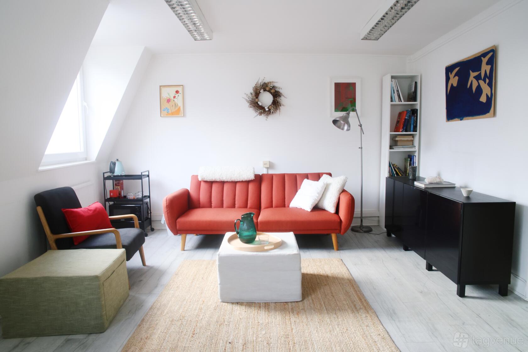 A rehearsal studio with a red sofa, armchair, wall art, and natural light in the Music Room at ICP London.