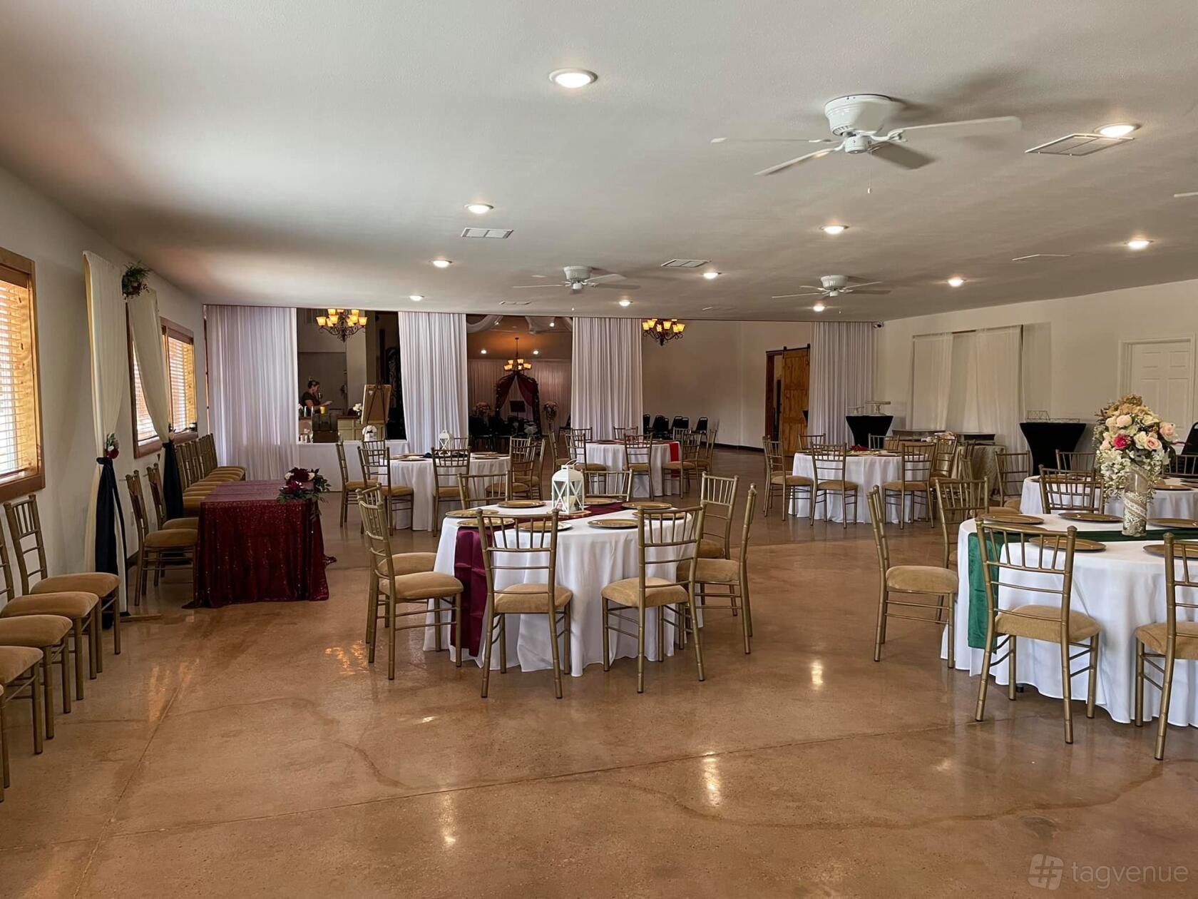 A banquet hall with round tables covered in white linens, gold chairs, and chandeliers at The Antonia Venue Banquet and Event Hall.