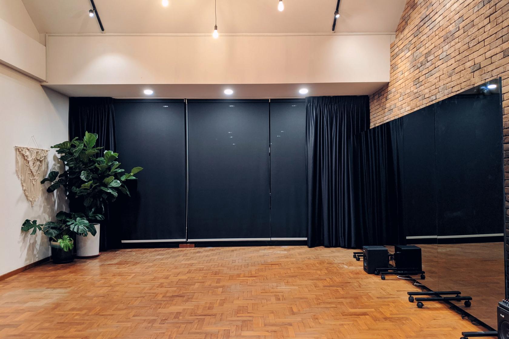 An event venue with parquet wood flooring, black-out curtains, track lighting, and a potted plant at The Common Good (TCG).