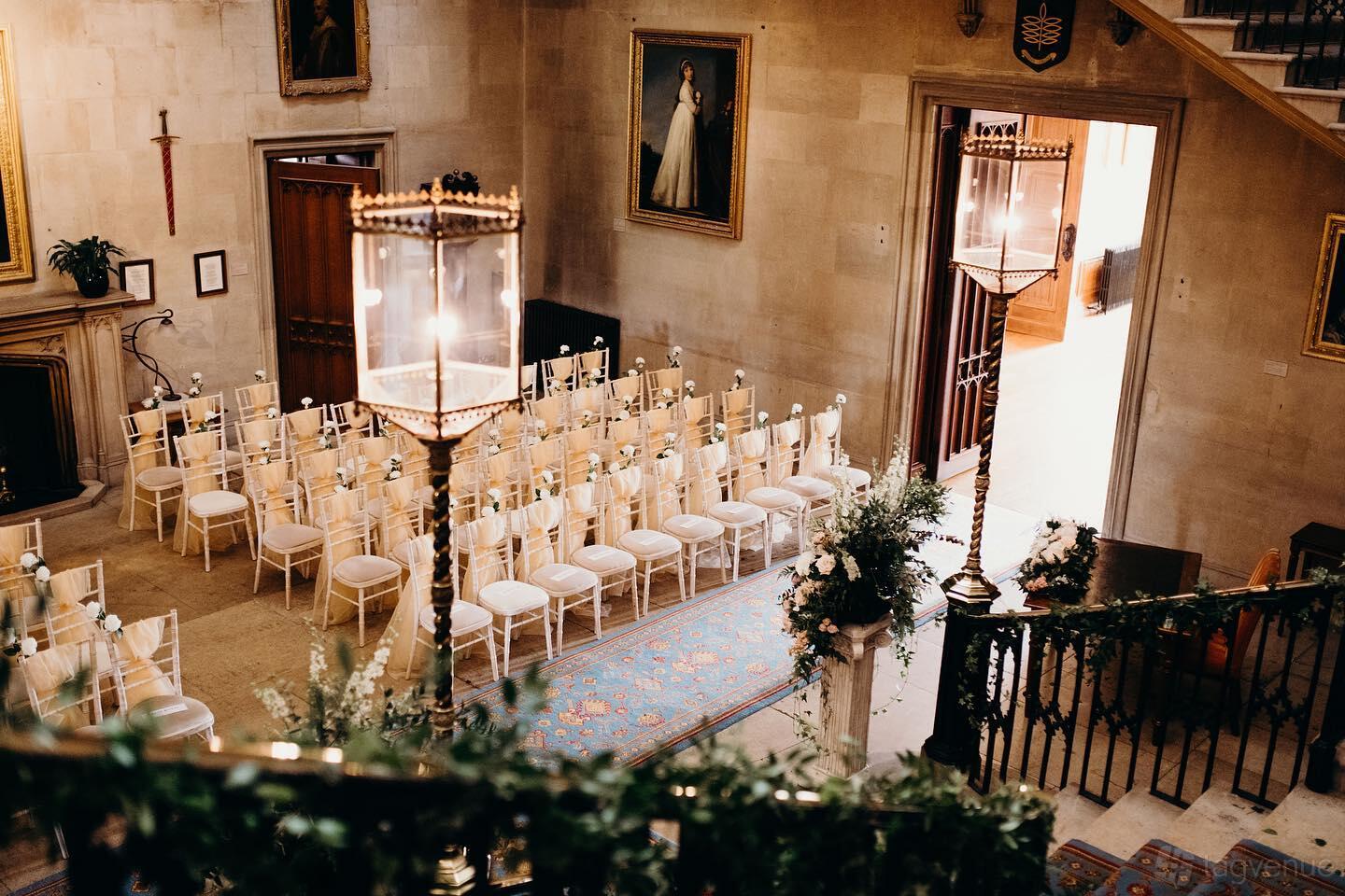 A castle hall with rows of ivory chairs on a patterned rug, ornate lighting, and stone walls at Ashridge House.