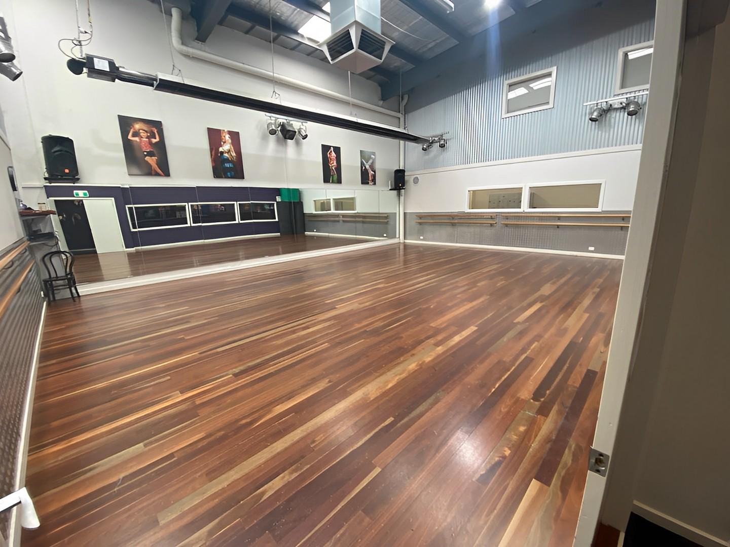 A rehearsal room with polished wood floors, wall mirrors, ballet barres, and dance posters at The Edge Performers School.