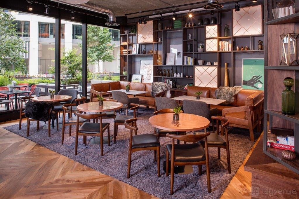 A bar with wooden tables, leather sofas, bookshelves, and floor-to-ceiling windows at Drake & Morgan at King's Cross.