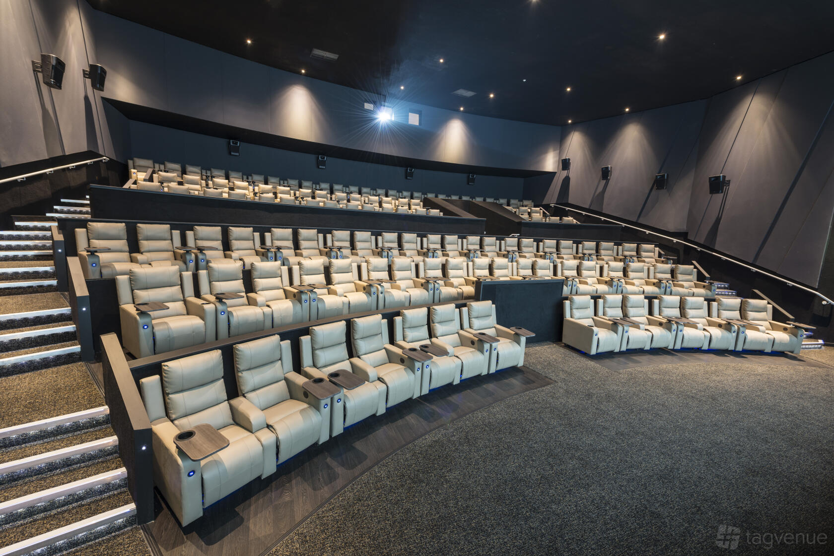 A cinema auditorium with tiered rows of reclining leather seats and illuminated stairways at ODEON LUXE Putney.