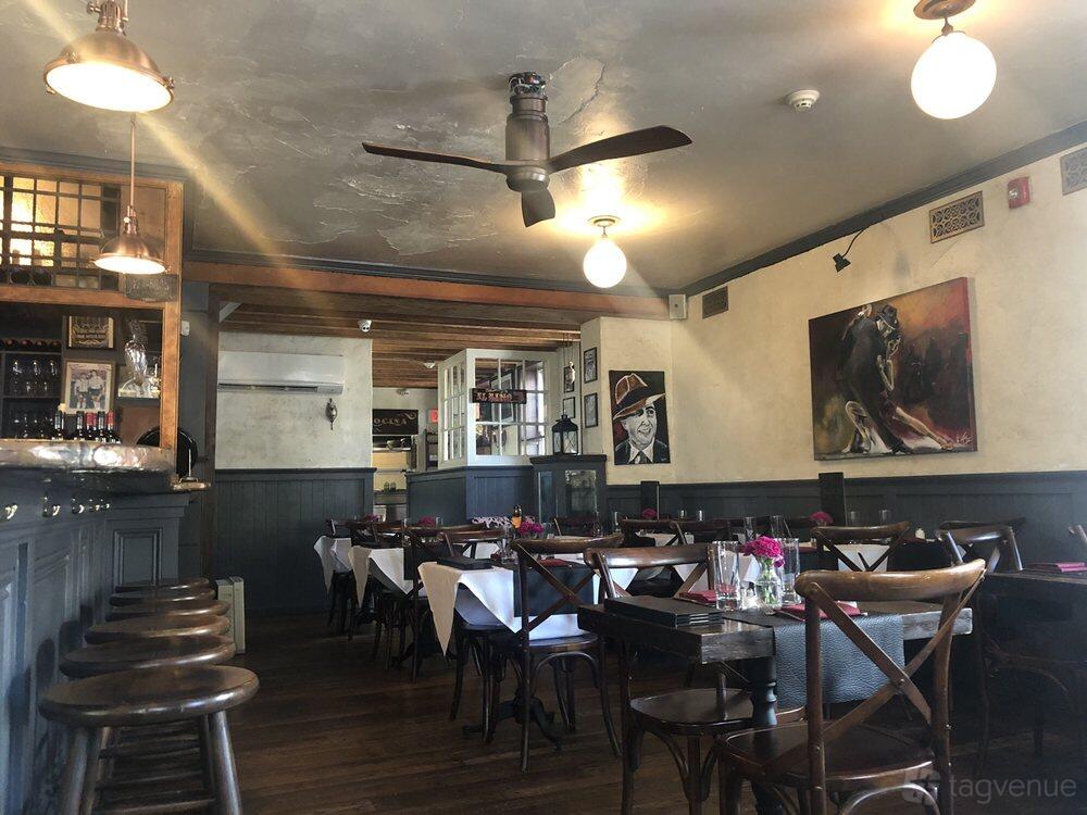 A restaurant dining area with wooden floors, dark paneled walls, white tablecloths, and art-lined walls at Malbec Steakhouse.