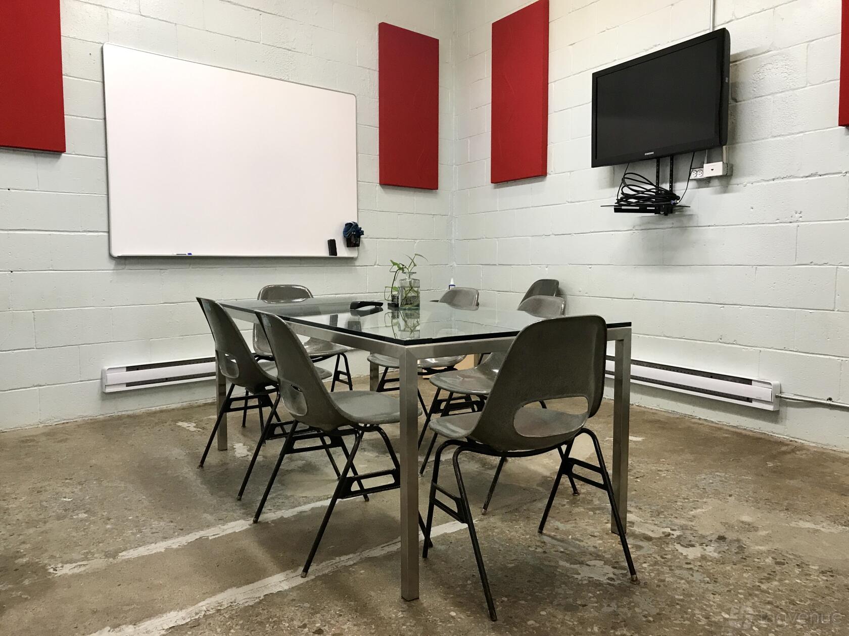 A meeting room with a glass table, six chairs, wall-mounted TV, and whiteboard at ACME Works.