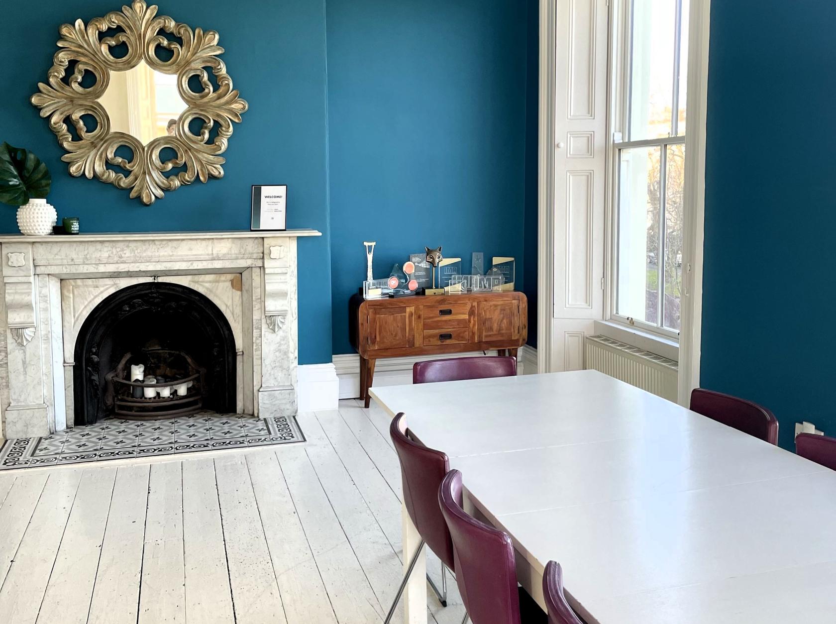 A boardroom with a white marble fireplace, blue walls, and a large window at Number Twelve.