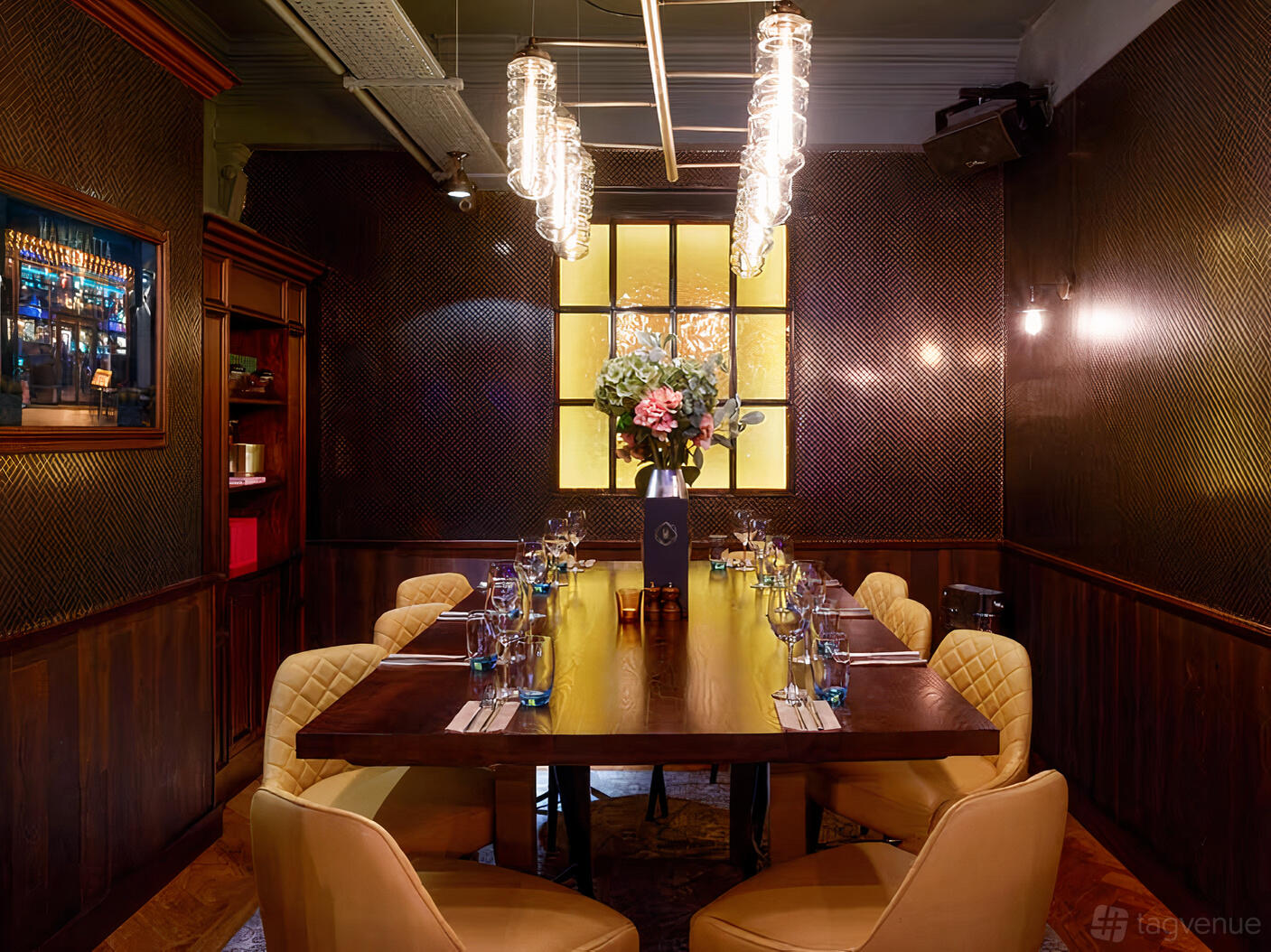 A dining room with a long wooden table, plush chairs, and decorative lighting at Manahatta Deansgate.