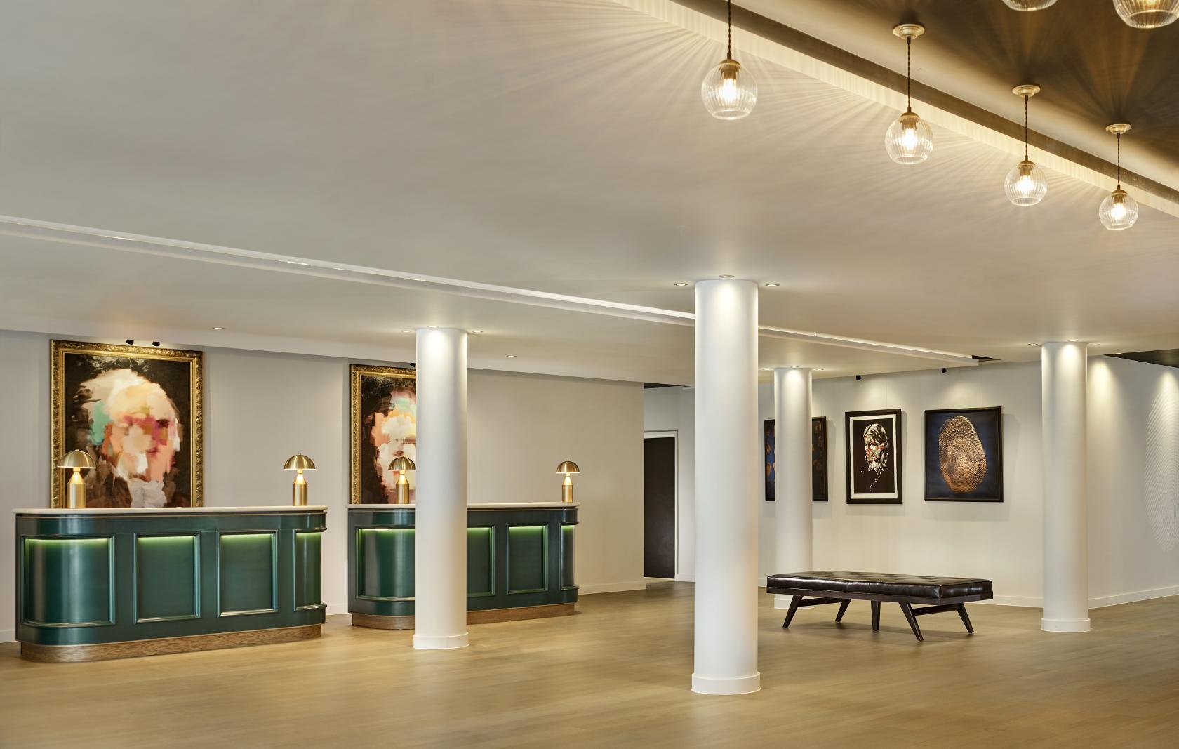 A hotel meeting area with green reception desks, framed artwork, and pendant lights at The Westminster London.