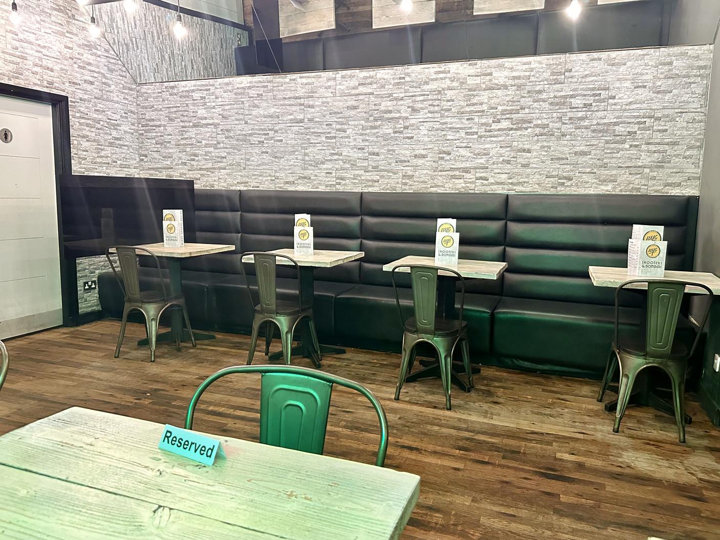 An event space in a bar with gray brick walls, black leather banquette seating, and wooden tables at NYC Bar & Grill.