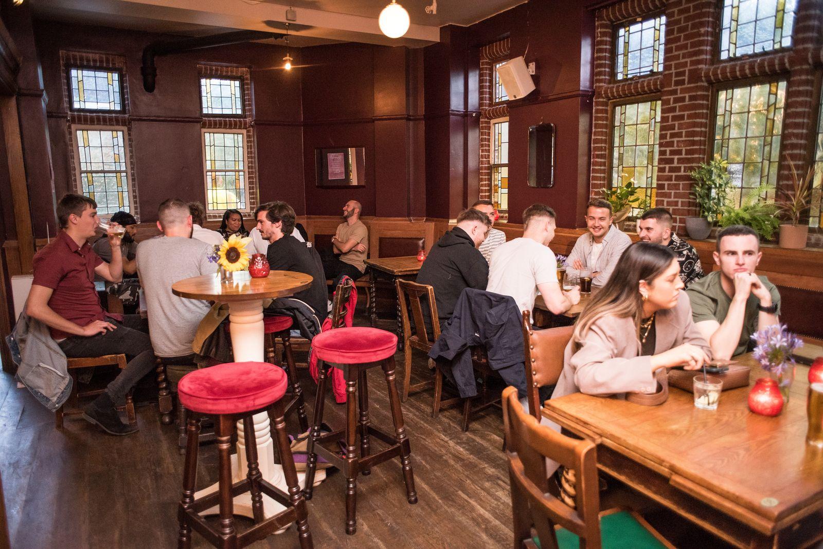 A pub with exposed brick walls, leaded glass windows, wooden tables, and high stools at Duke of Edinburgh.