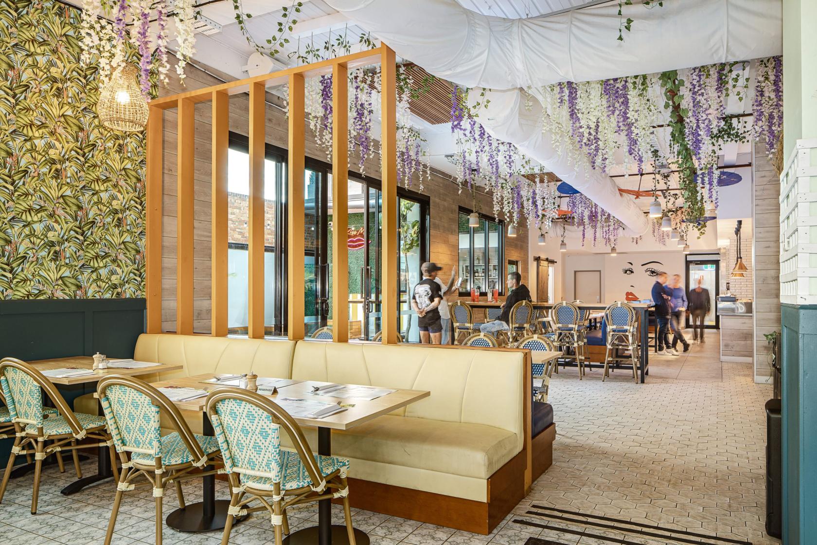 A dining room with floral wallpaper, hanging wisteria, and rattan chairs at The Bungalow Beer Garden.