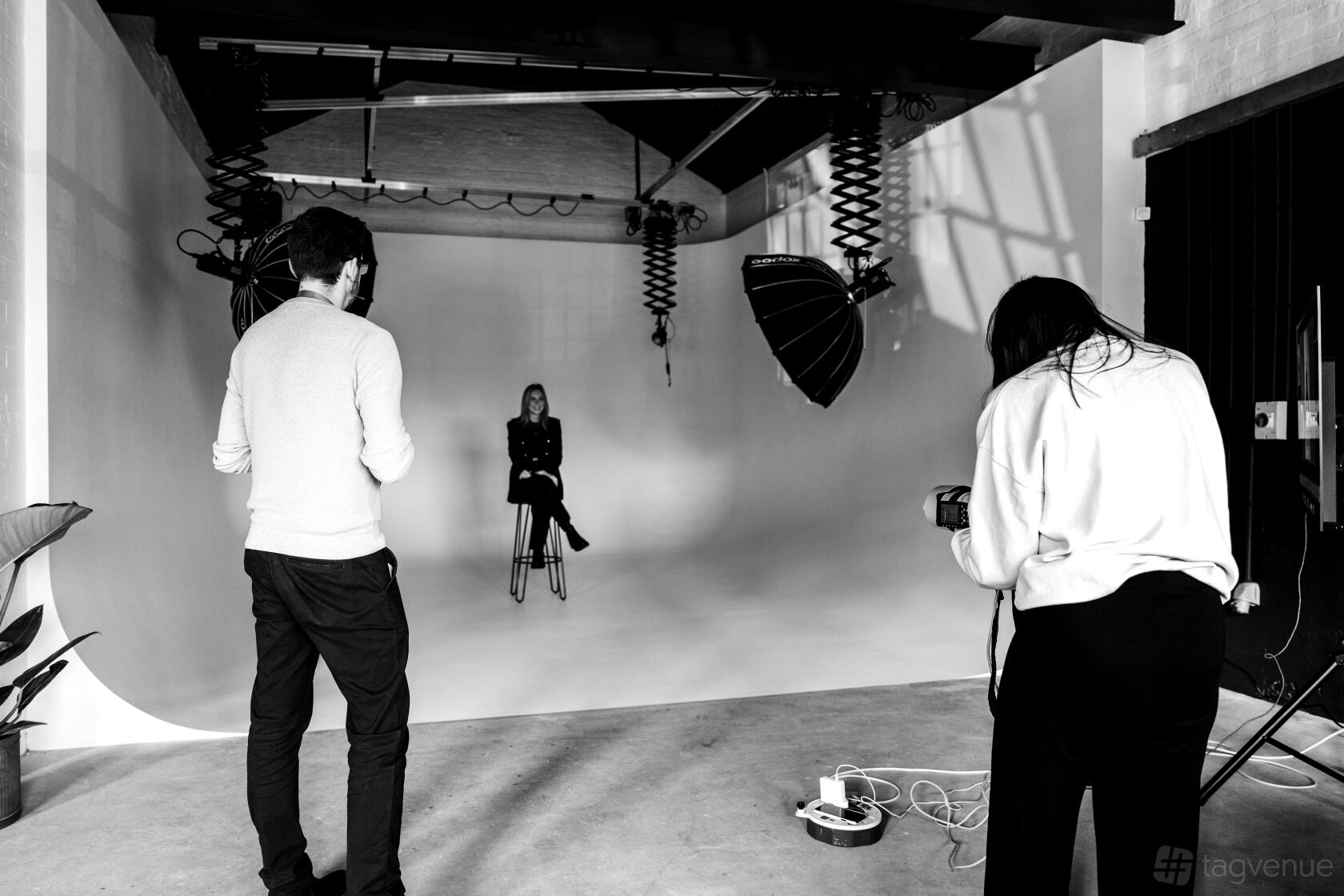 A photo studio with a white infinity cove, mounted studio lights, and a seated subject at Flux Studio.