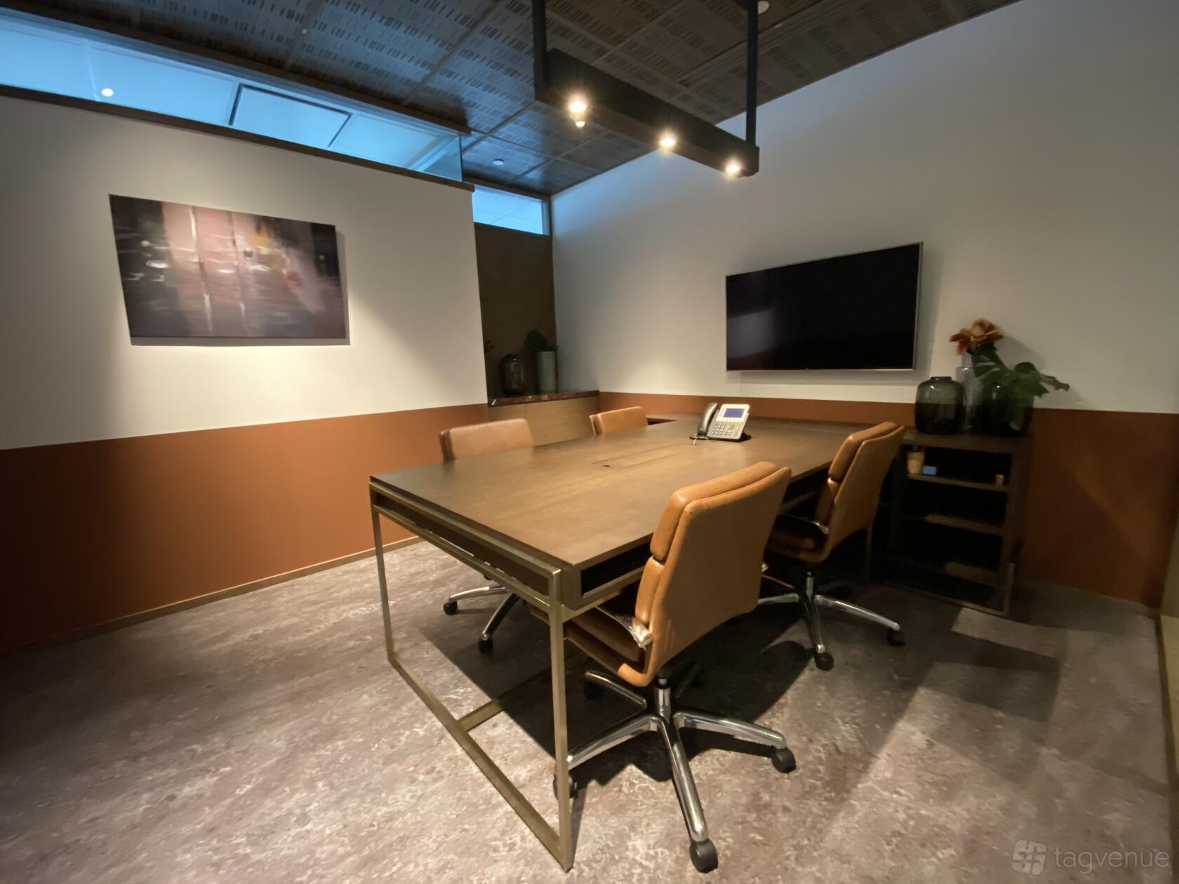 A meeting room with a wooden table, four leather chairs, wall-mounted screen, and soft lighting at The Great Room - Centennial Tower.