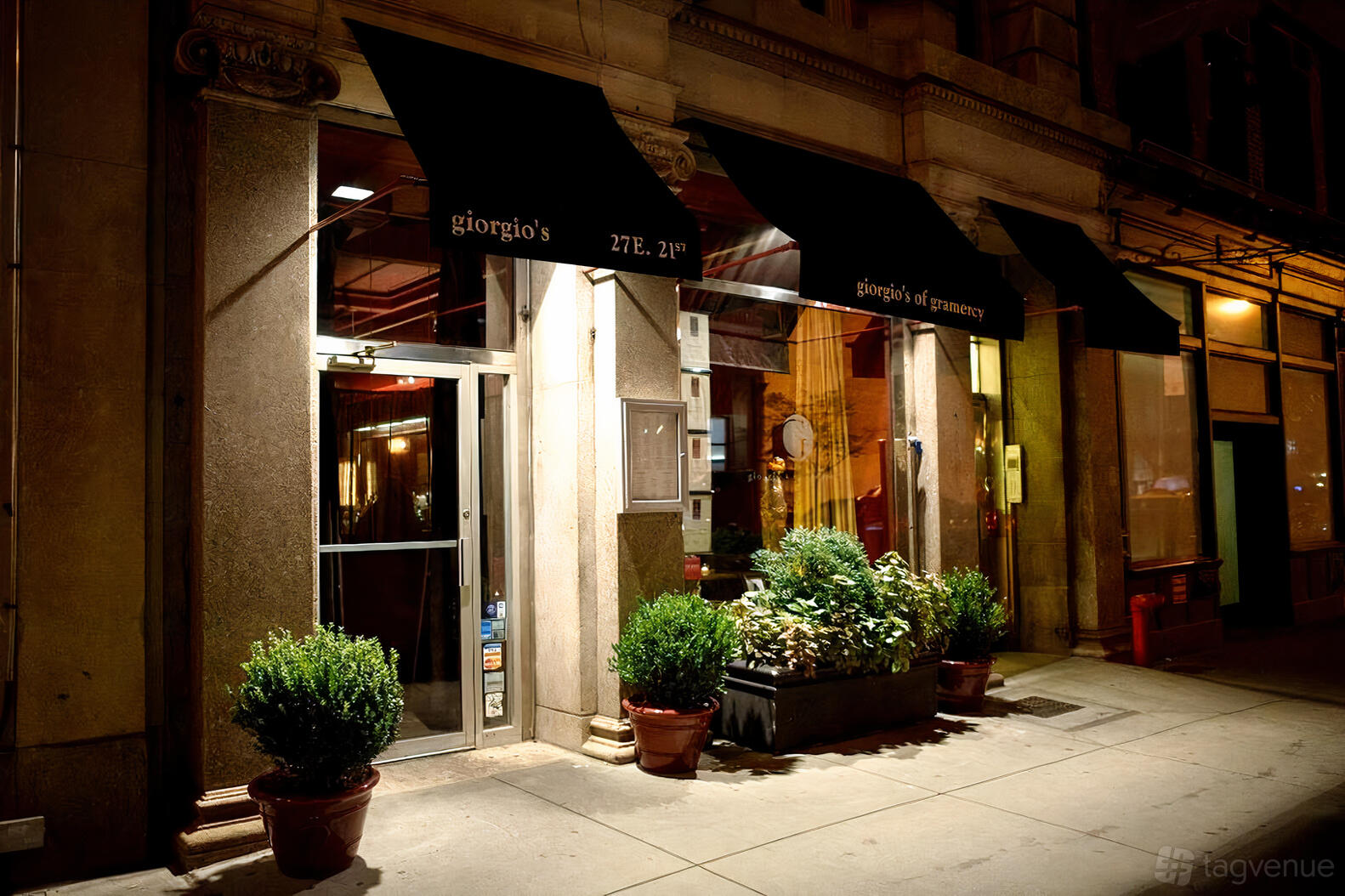 A restaurant entrance with black awnings, glass doors, and potted plants at The Flatiron Room @ Giorgio's of Gramercy.