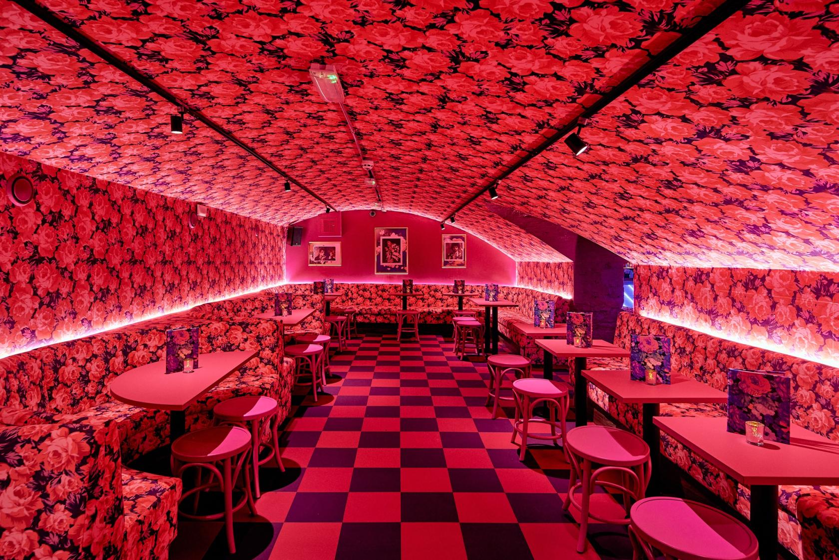 A bar with floral wallpaper, checkerboard flooring, and pink seating in the Pink Rose Room at Blame Gloria Bristol.