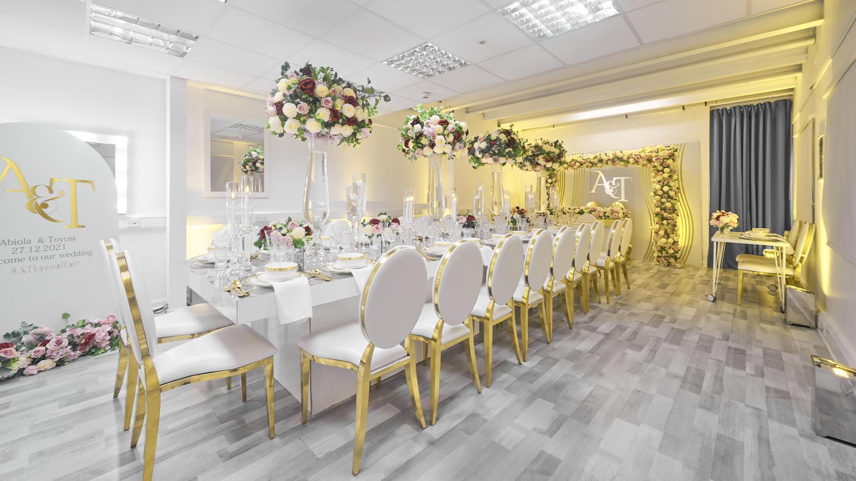 An event space with banquet seating, gold-trimmed white chairs, tall floral centerpieces, and soft lighting at UniQ Royal Arsenal.