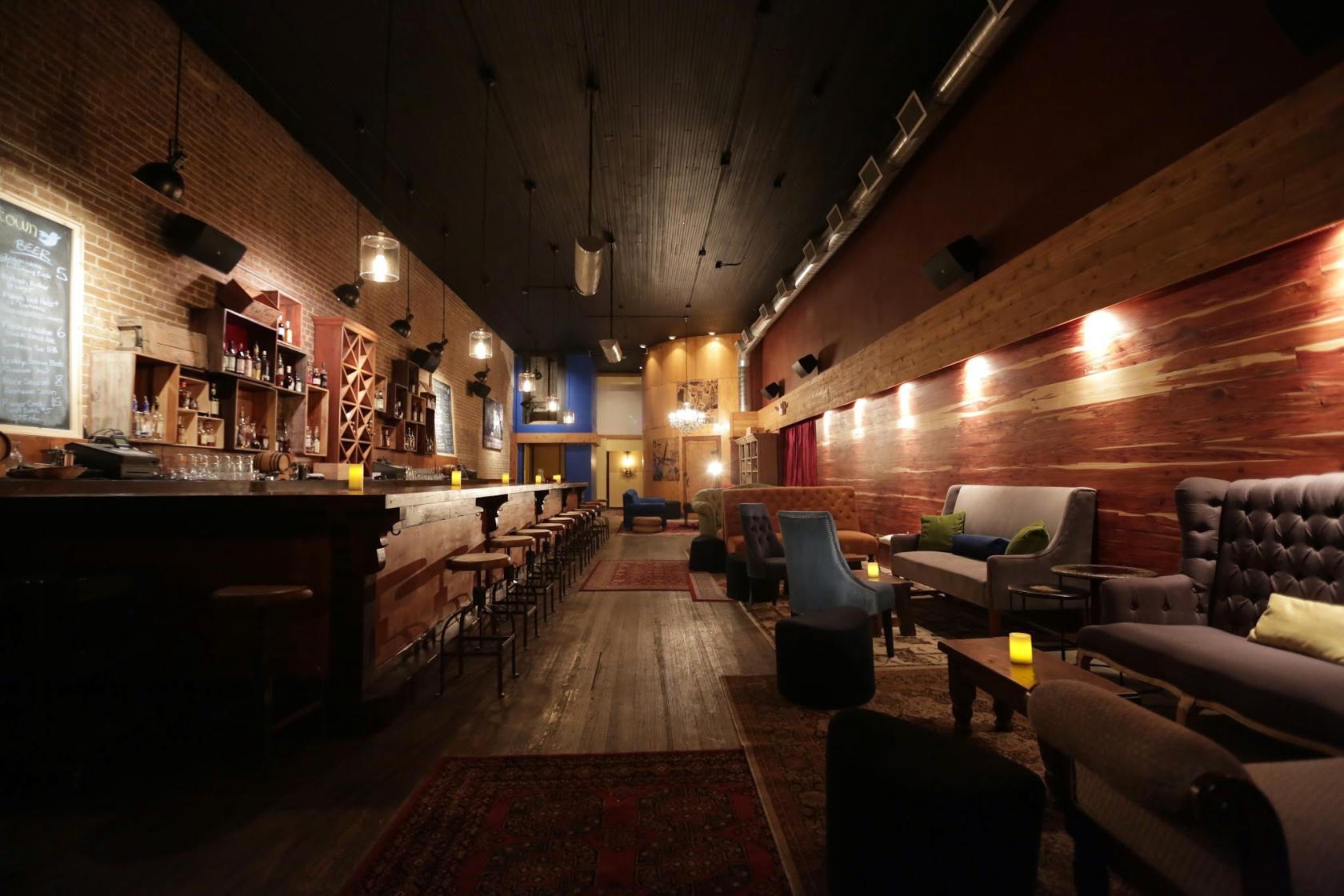 A bar with exposed brick walls, wood paneling, vintage rugs, and eclectic lounge seating at Dean's Downtown.