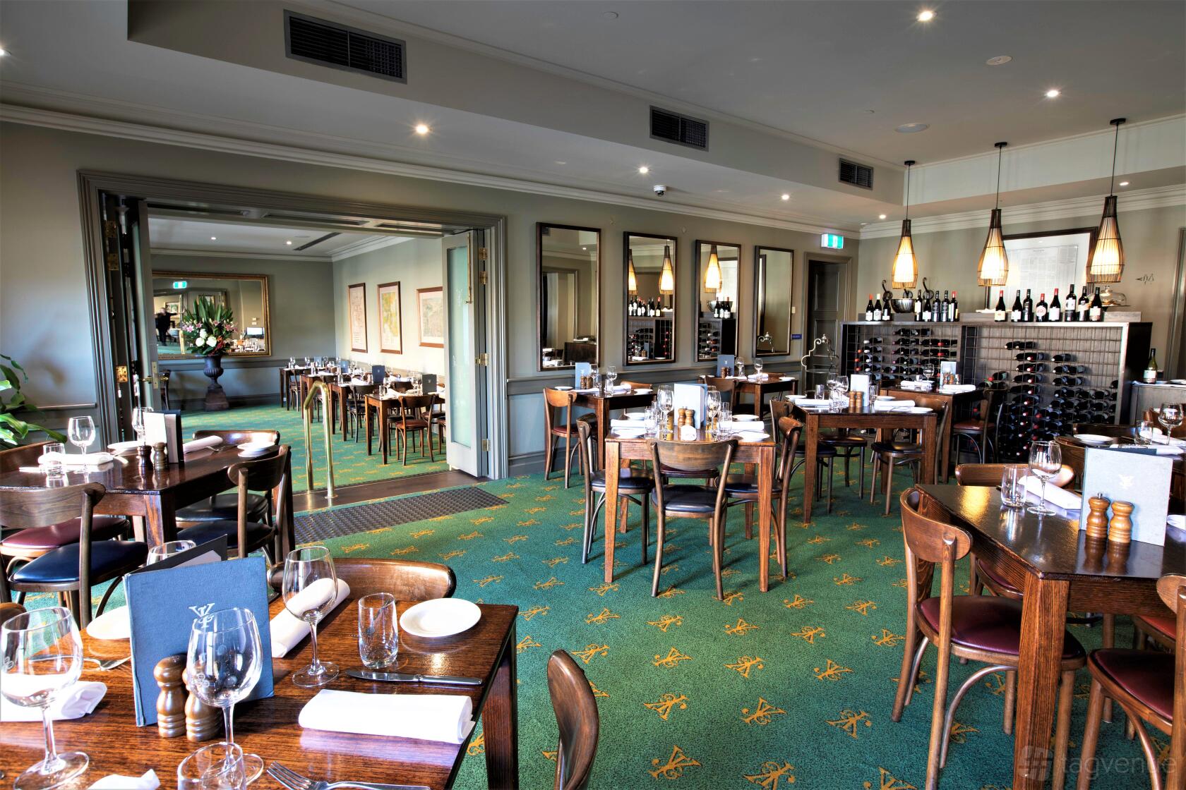 A pub dining room with green patterned carpet, wooden tables set with glassware, and pendant lighting at Young & Jacksons.