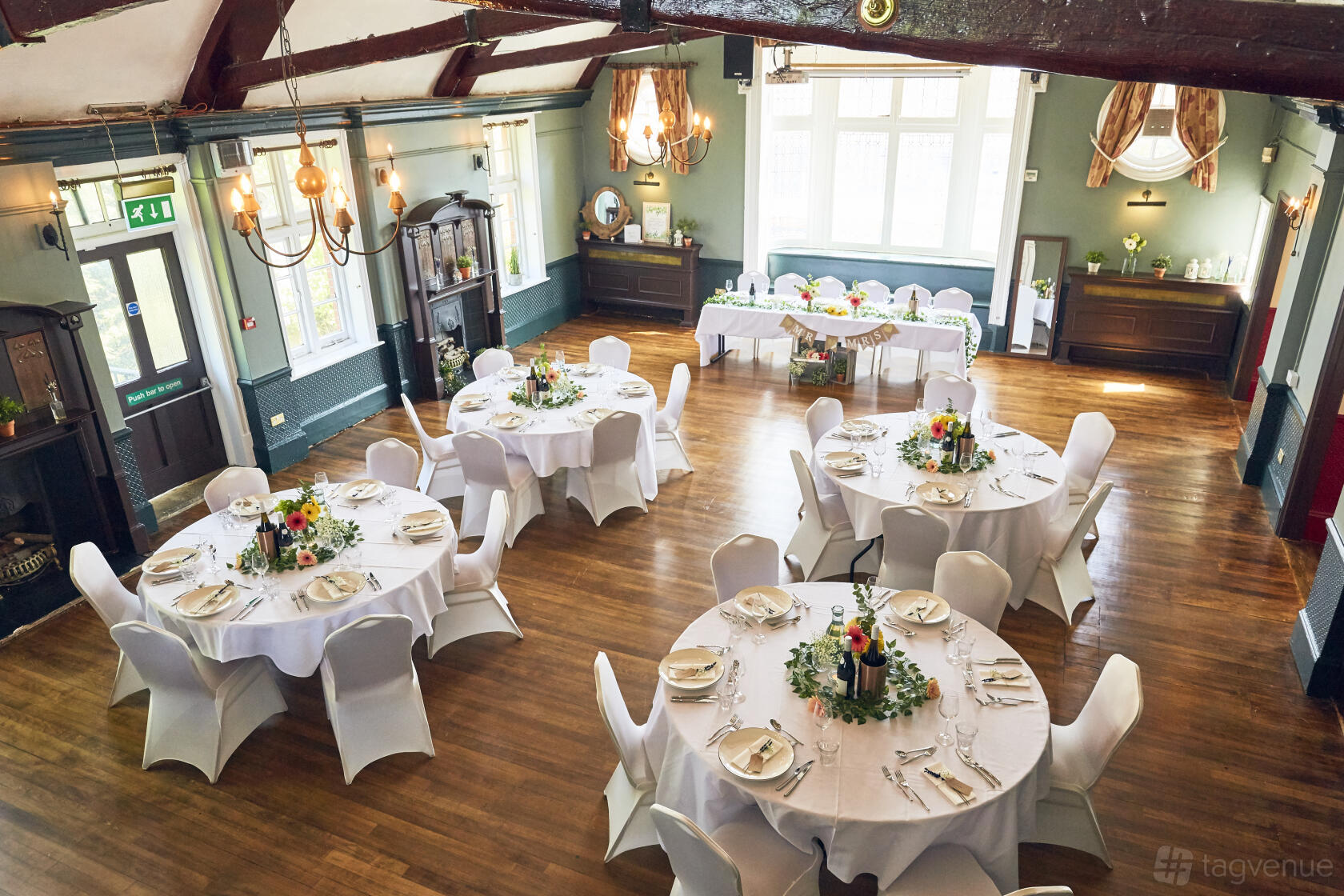 An event space with round tables dressed in white linens, wooden floors, and large windows at The Royal Oak.