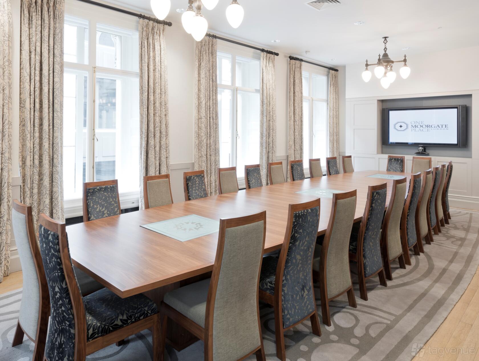 A boardroom with a long wooden table, high-back chairs, large windows, and a mounted display screen at One Moorgate Place.