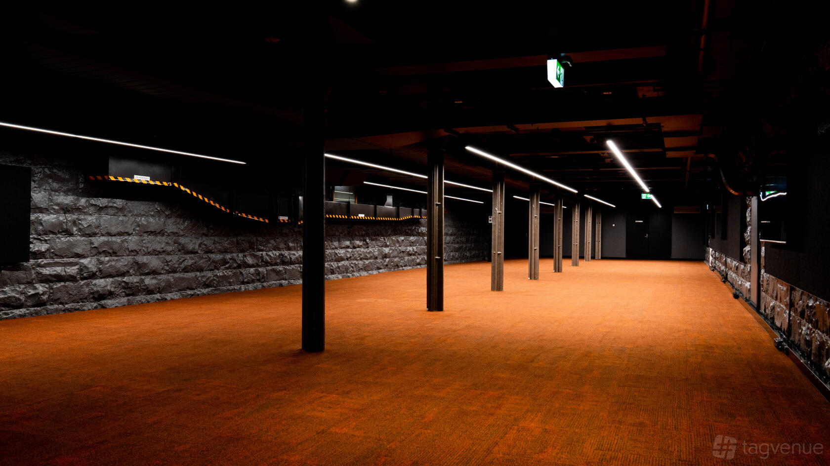 A basement with exposed stone walls, orange carpet, and linear ceiling lights at Stone & Chalk Melbourne.