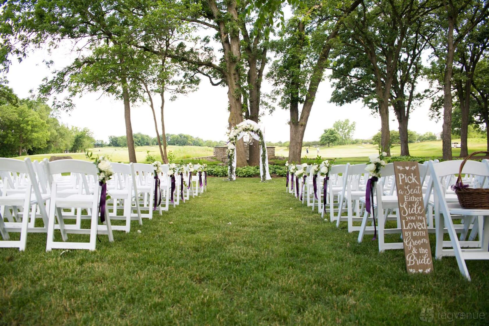 An outdoor ceremony area with white folding chairs, floral decorations, and a wooden archway at Stonebridge Country Club.