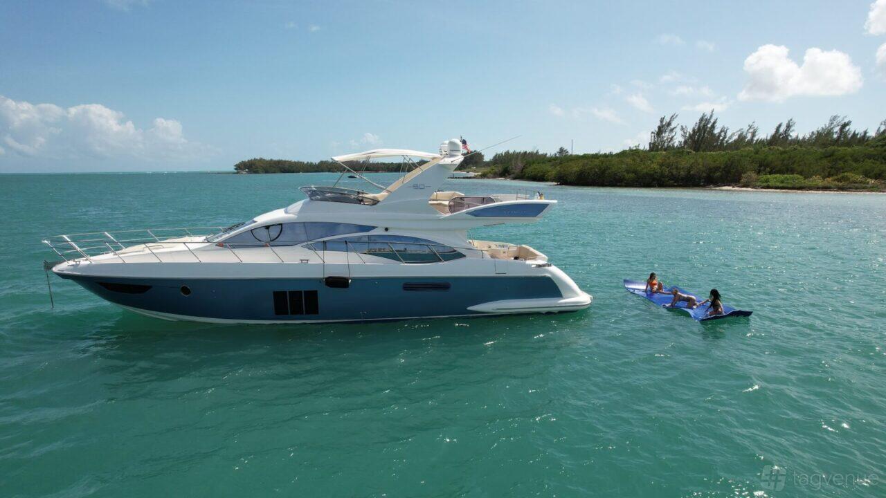A yacht with a sun deck and flybridge sailing on turquoise water near kayakers at Pearl Yacht Charters.