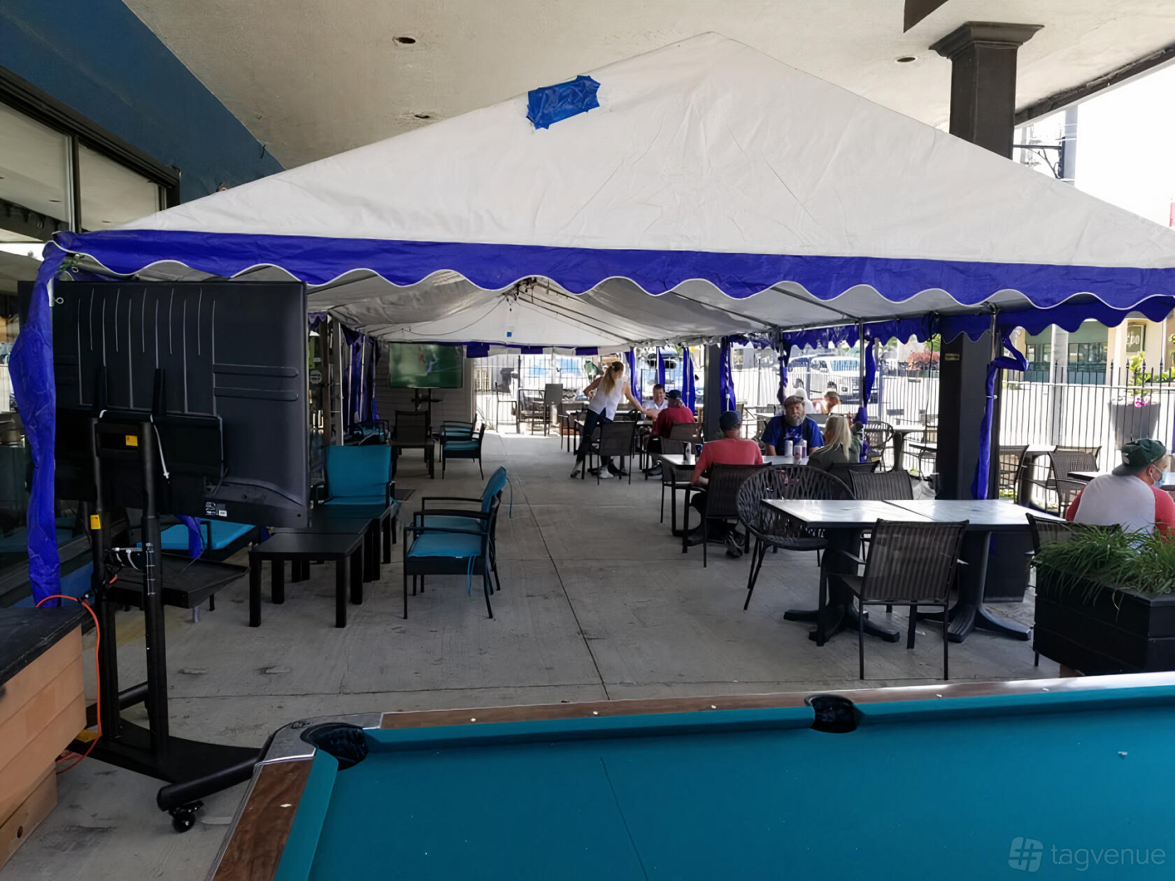 An outdoor terrace with a white canopy, lounge chairs, dining tables, and a pool table at Maple Leaf House Grill & Lounge.