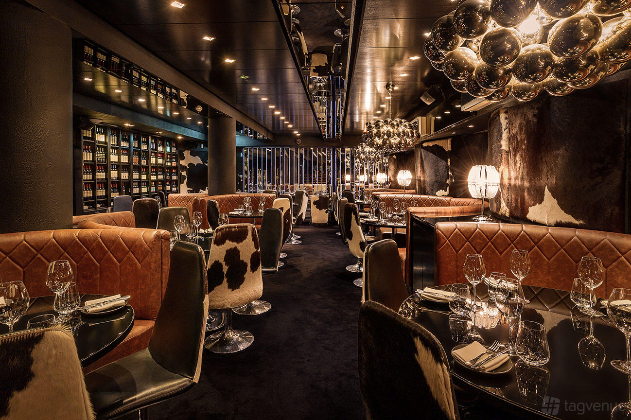A restaurant with cowhide upholstery, round tables set with glassware, and sculptural lighting at Gaucho Sloane Avenue.