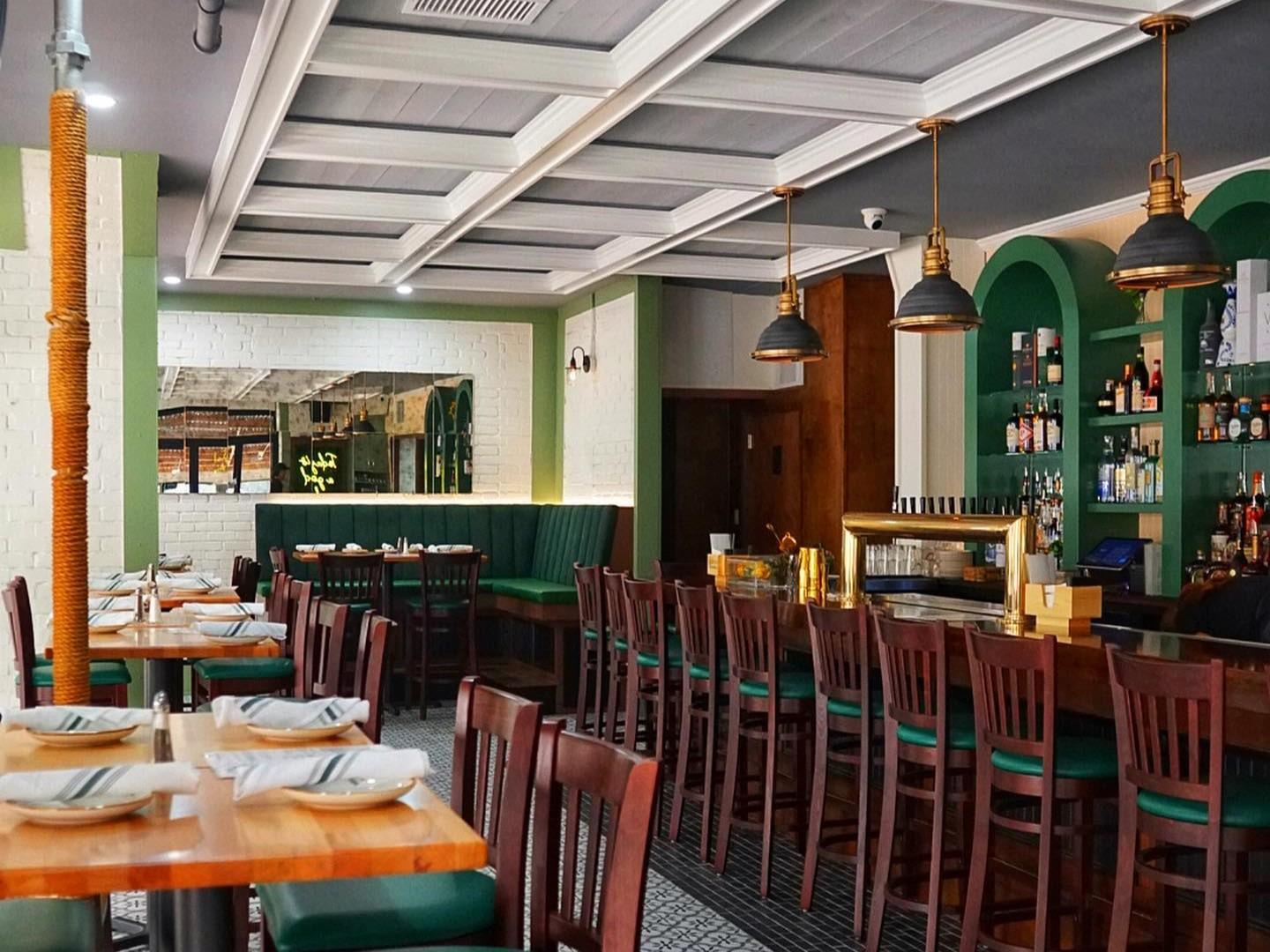 A bar with a long wooden counter, upholstered green bench seating, and pendant lights at The Laurels.