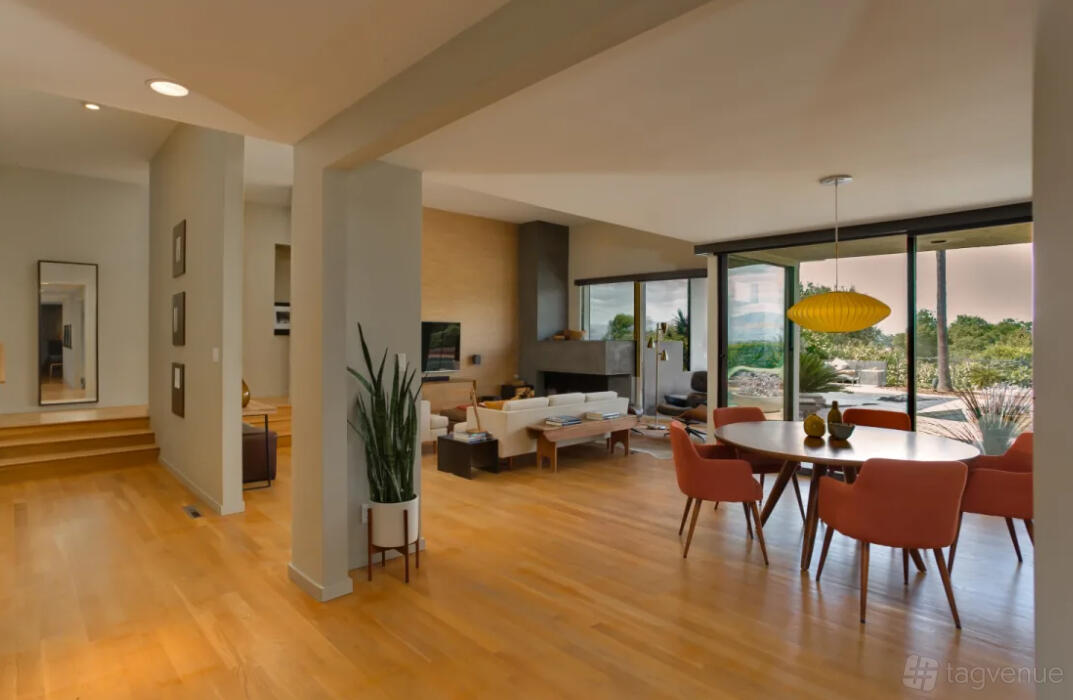 An open-plan house with wood floors, a round dining table with pink chairs, and floor-to-ceiling windows at Warm & Modern House.
