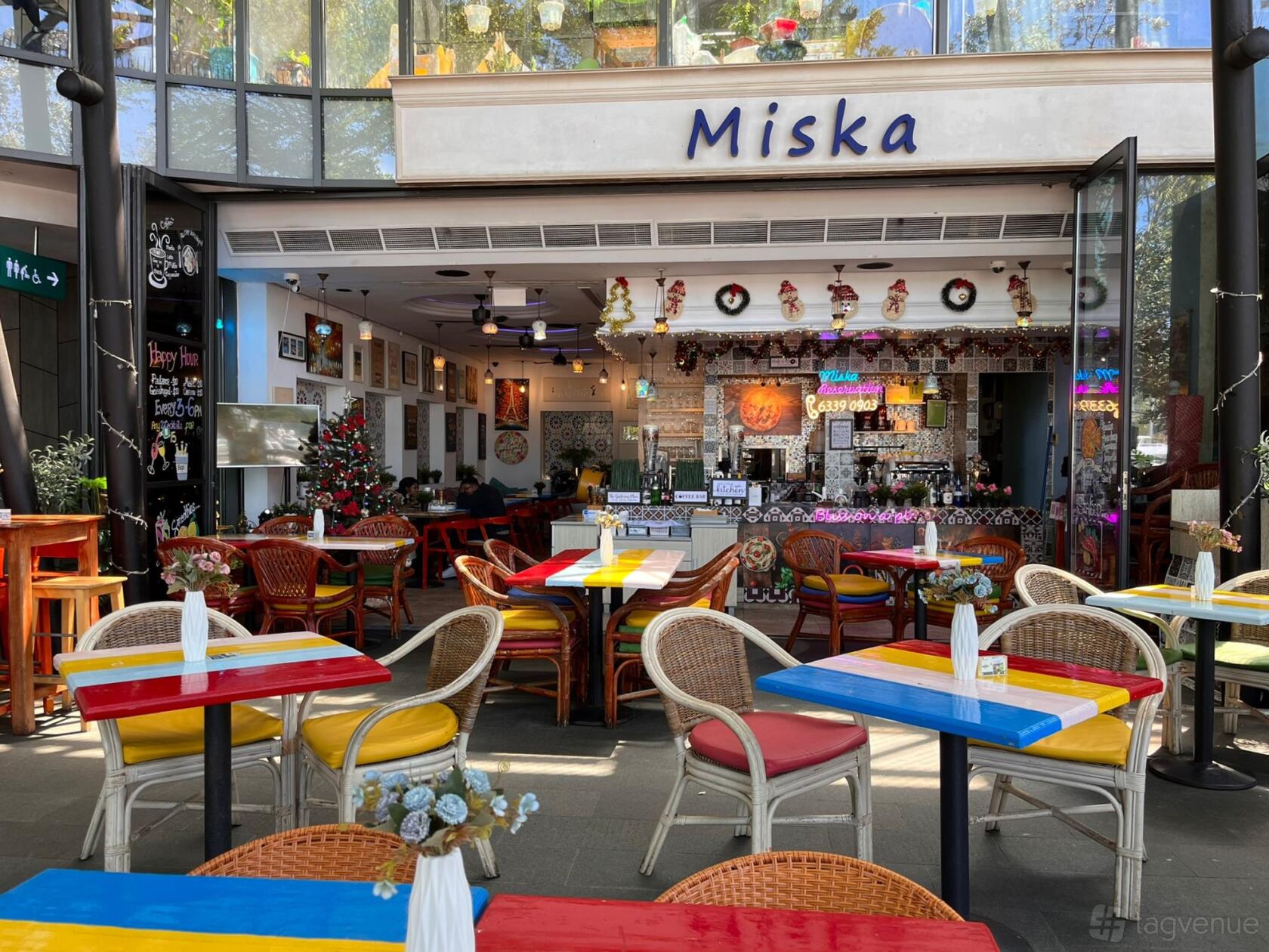 An outdoor restaurant seating area with colorful tables and woven chairs at Miska Cafe.