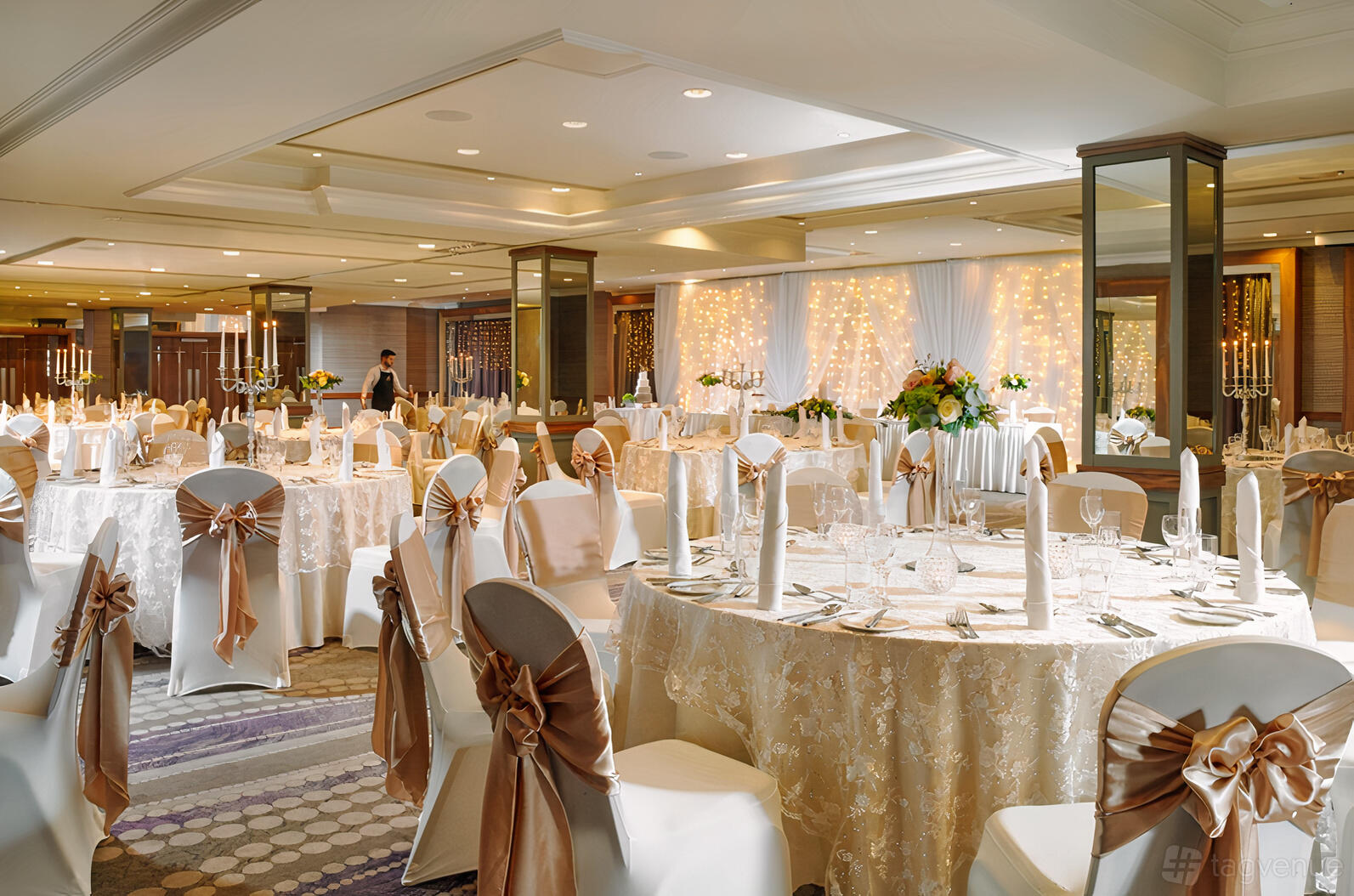 An event space with round tables dressed in lace linens, chair sashes, and fairy lights at The Malone Hotel.