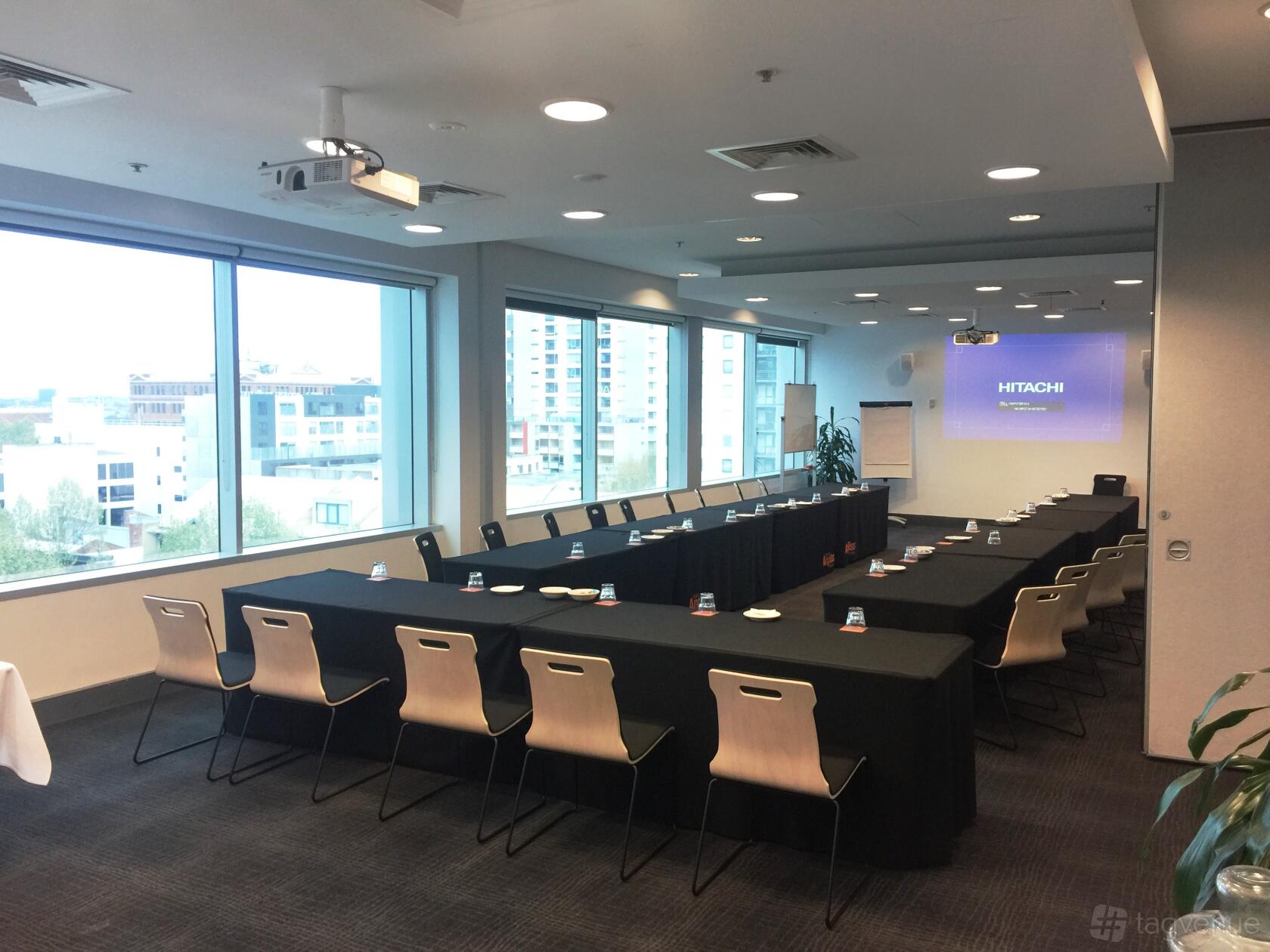 A meeting room with floor-to-ceiling windows, U-shaped tables, and a ceiling projector at The Angliss Conference Centre.