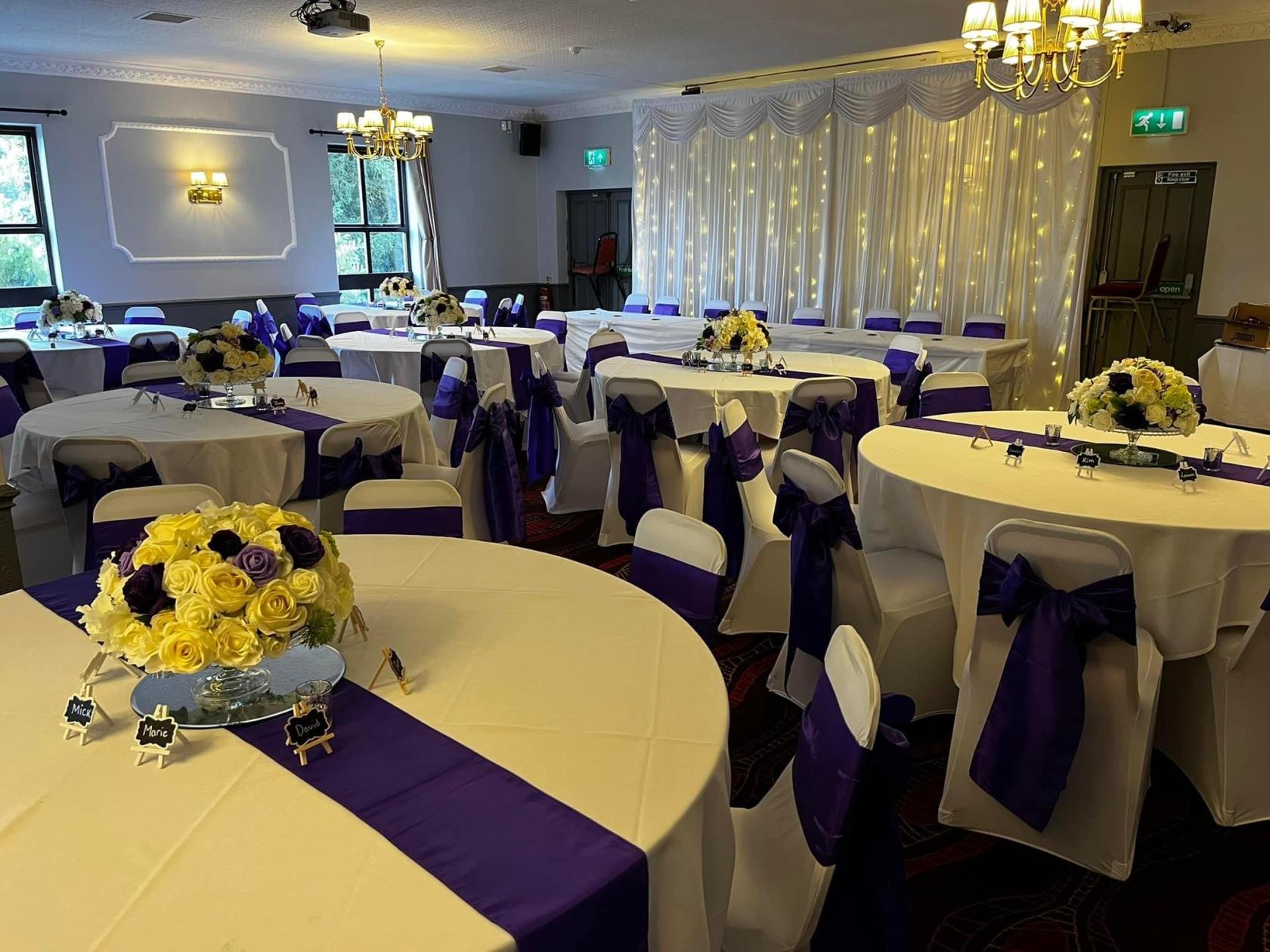 A pub function room with round tables dressed in white linens, purple sashes, and floral centerpieces at Ridgeway Arms.