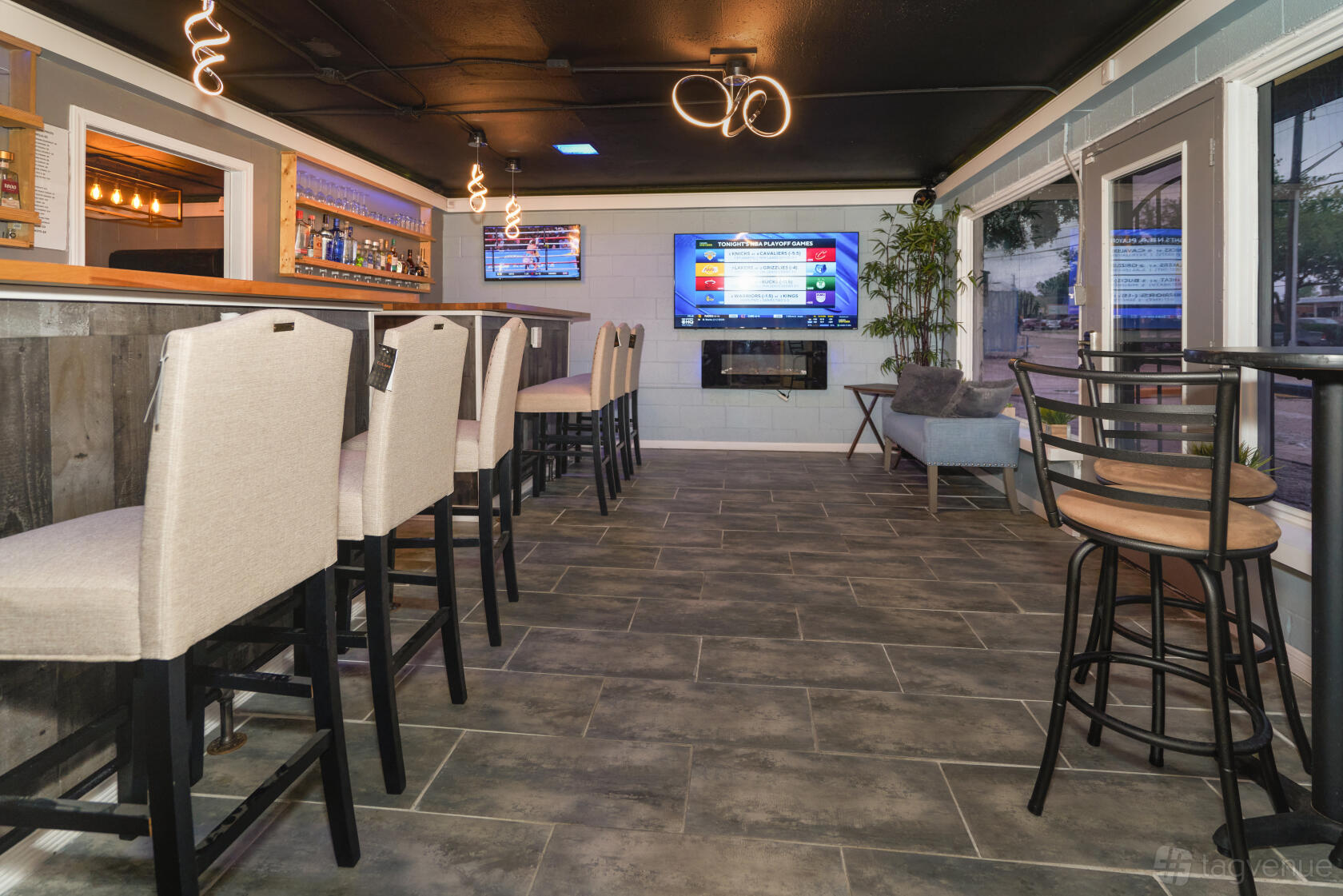A lounge with a long wooden bar, upholstered barstools, wall-mounted TV, and modern lighting at BCE Studios.