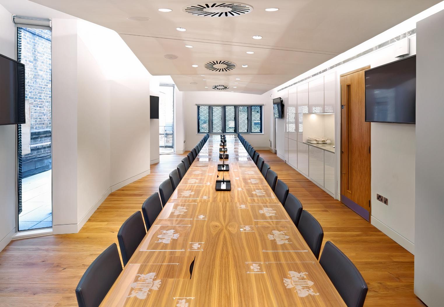 A meeting room with a long wooden conference table, black chairs, and floor-to-ceiling windows at The Royal College of Ophthalmologists.