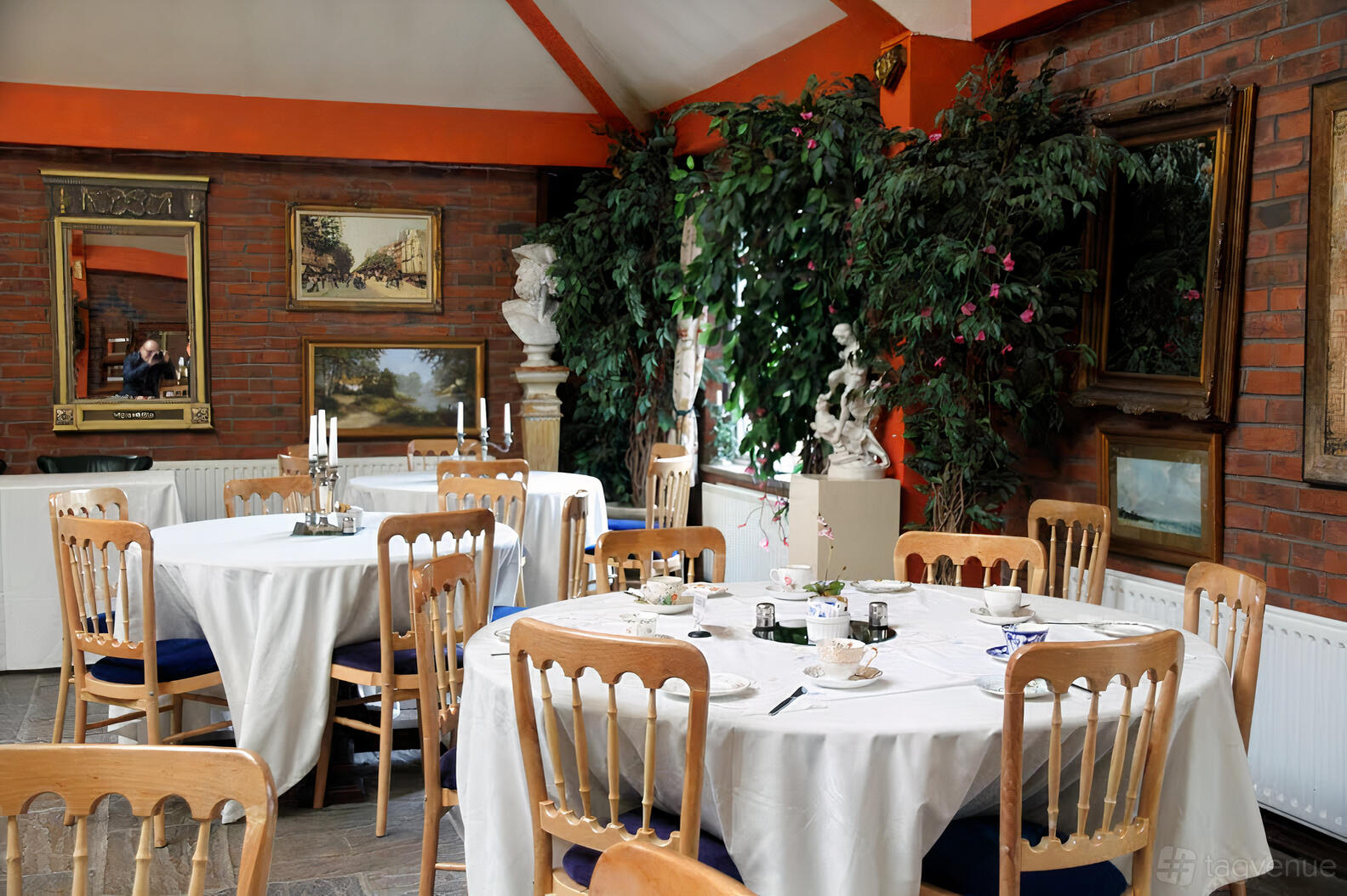 An event space in a hall with round tables draped in white linens, wooden chairs, and brick walls at Heskin Hall.