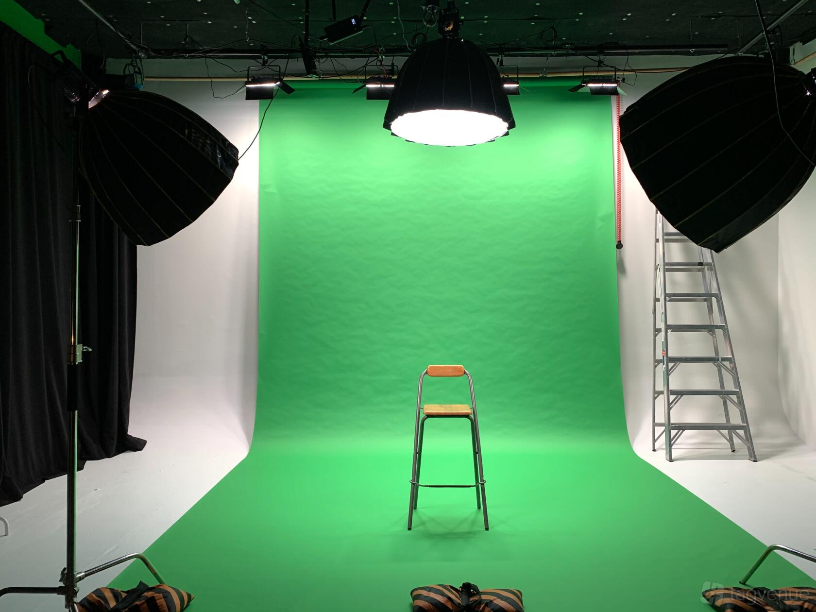 A photo studio with a green screen backdrop, central stool, large softbox lights, and ladder at La Fauna Studio.