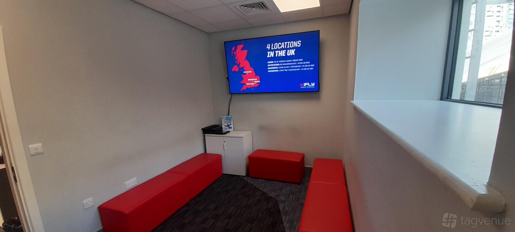 A meeting room with red bench seating, a wall-mounted screen, and carpeted floors at iFLY Indoor Skydiving at The O2.