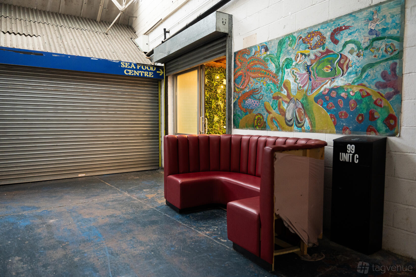 A versatile event space with a red leather sectional sofa, large mural, and exposed concrete floor at 6 Degrees studio.